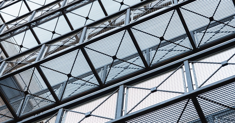 AI deployment governance: perforated metal mesh enclosing a steel walkway between two buildings