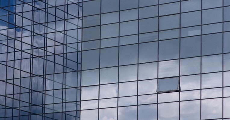 AI transparency requirements: a glass curtain wall reflecting open sky, its interior invisible from outside